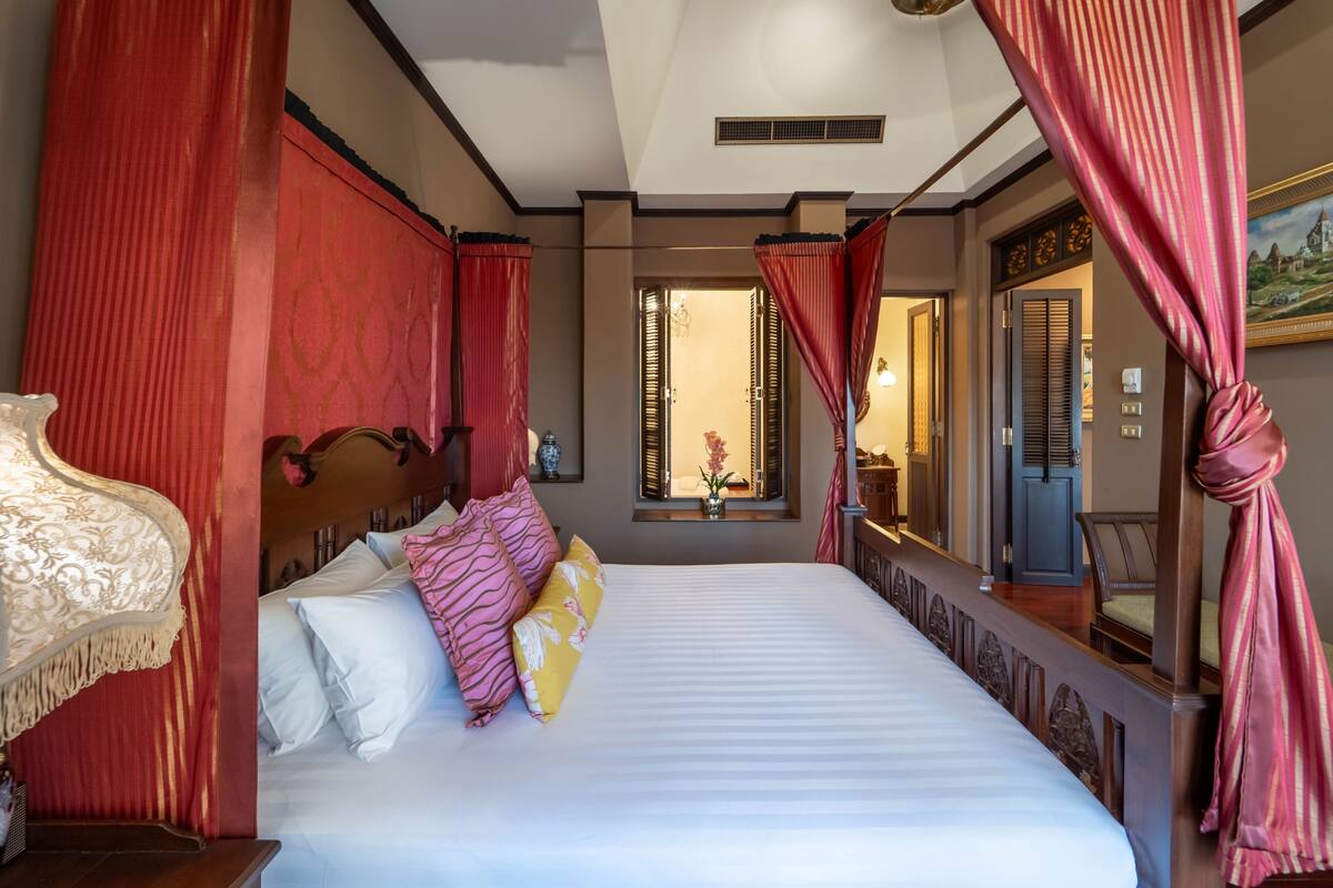Ein Hotelzimmer mit einem großen Bett, roten Vorhängen, einem Spiegel und Blick ins Innere.