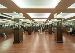 A gym with mirrored walls, wooden flooring, and various exercise equipment.