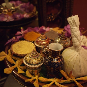 A variety of ornate containers and a white cloth on a wooden tray, surrounded by purple flowers.
