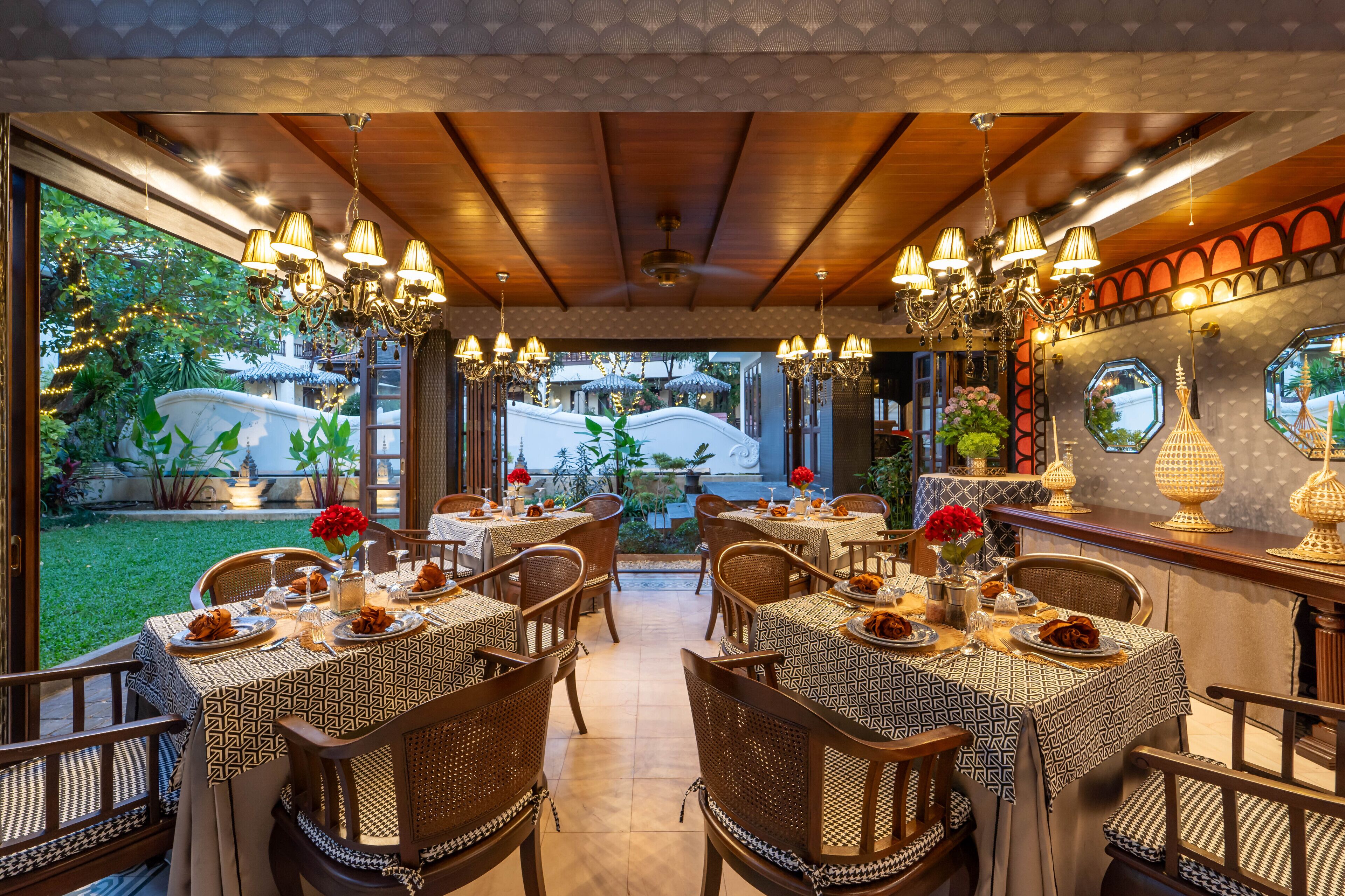 A restaurant with outdoor seating, wooden tables, wicker chairs, and hanging chandeliers.