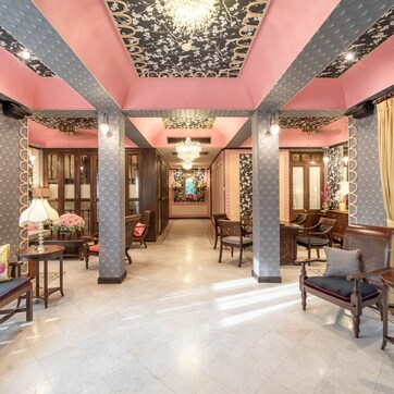 A luxurious hotel lobby with a pink and black color scheme, featuring ornate columns, chandeliers, and elegant furniture.