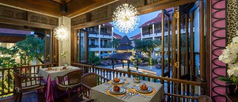 A dining area with tables set for two, wooden chairs, and a chandelier.