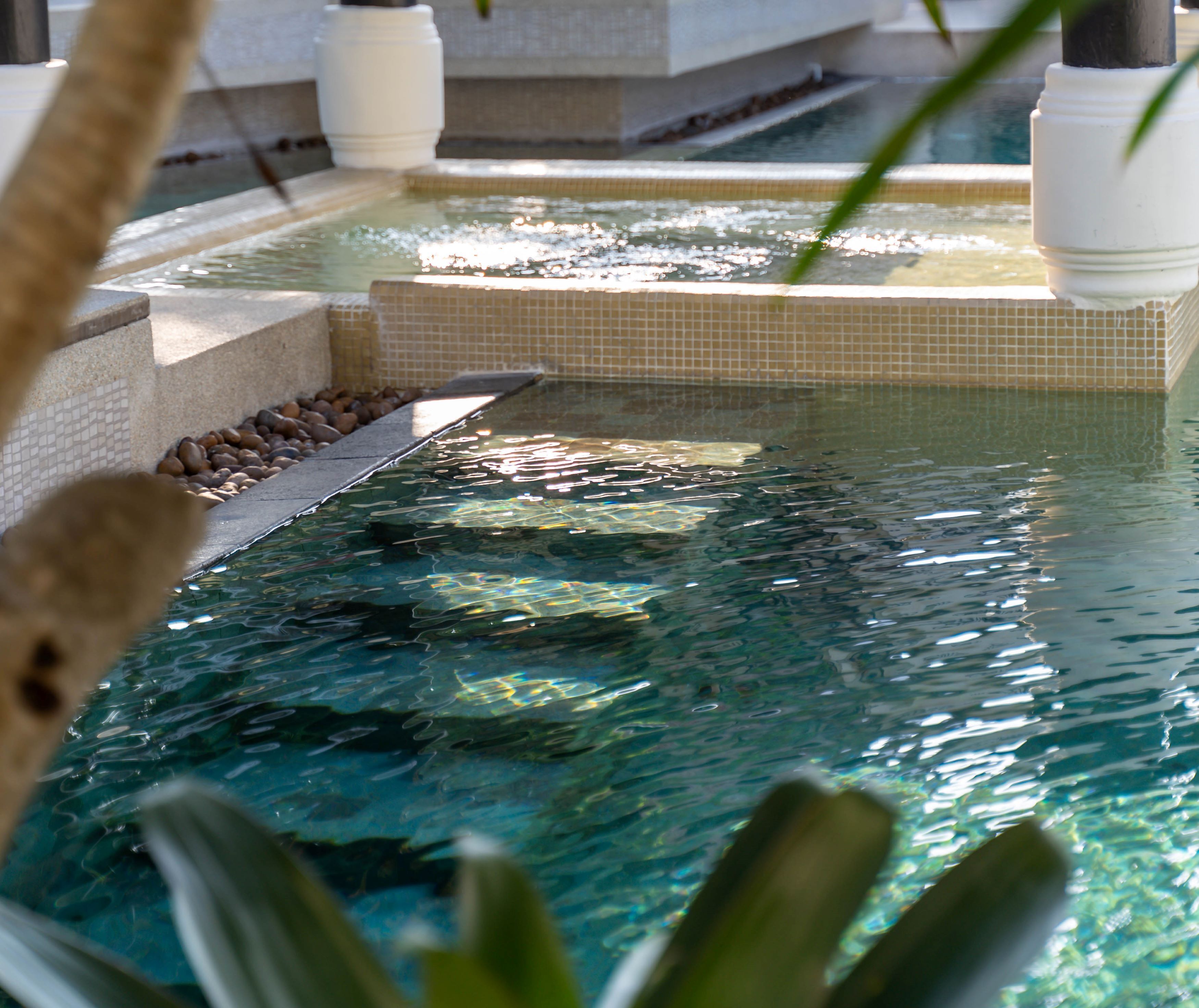 A pool with clear water, tiled edges, and a pebble-lined walkway.
