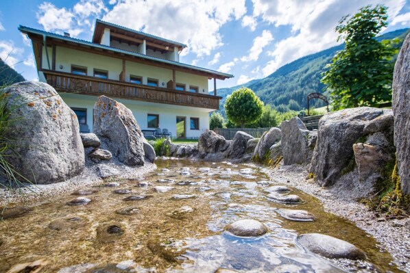 A mountain lodge with a stone pathway leading to the entrance, surrounded by large boulders and a clear view of the mountains.