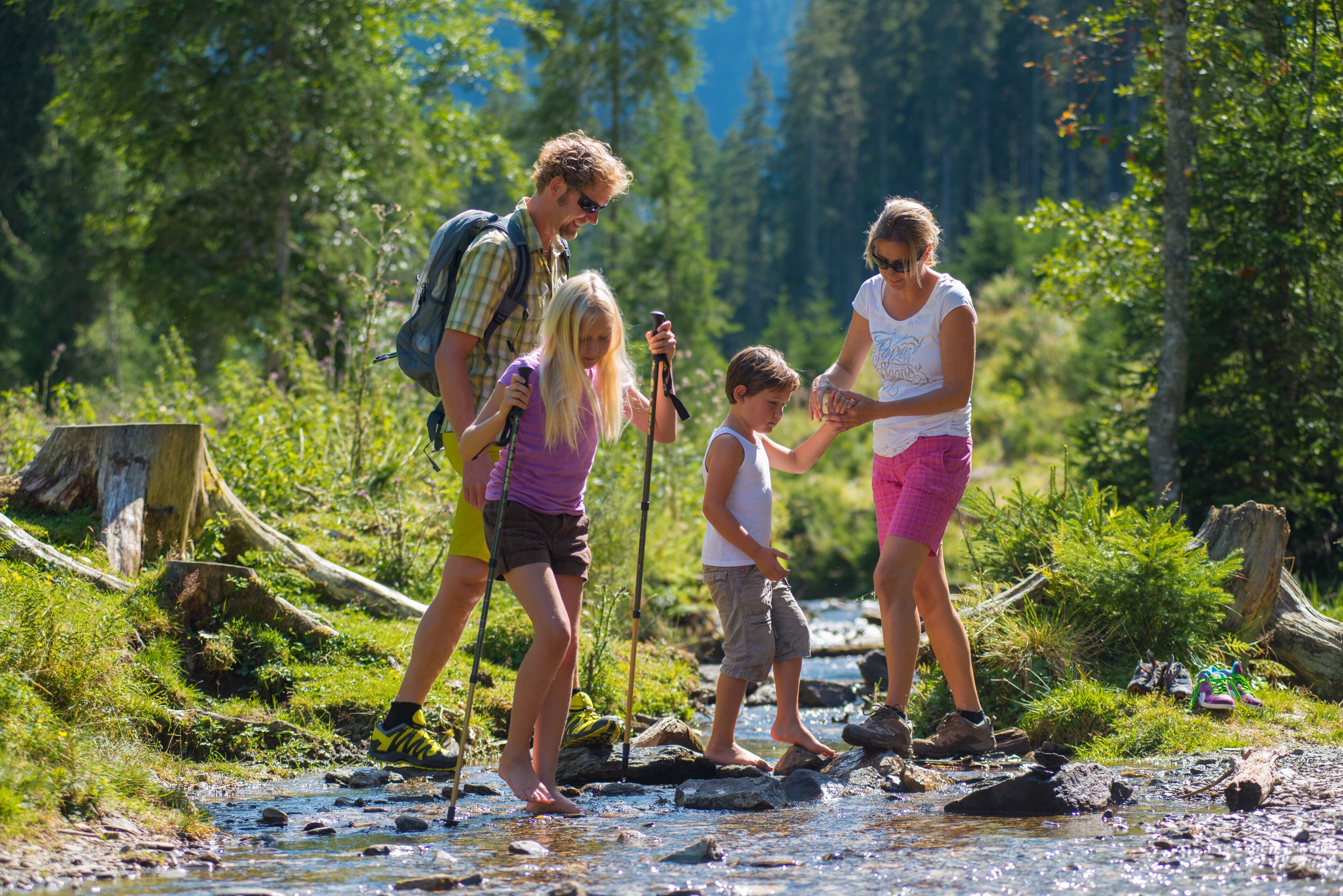 A family crossing a shallow stream in a forested area.