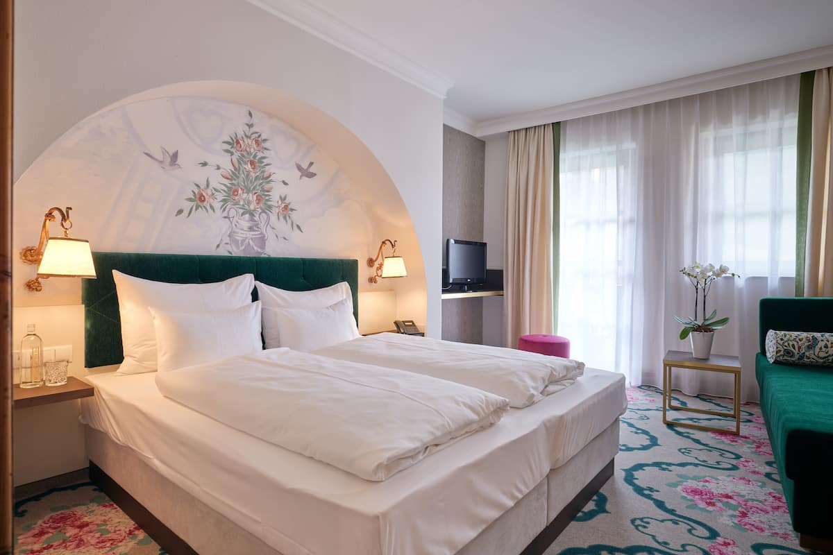 A hotel room with a large bed, two bedside tables, a television, a small side table with a plant, and a green sofa.