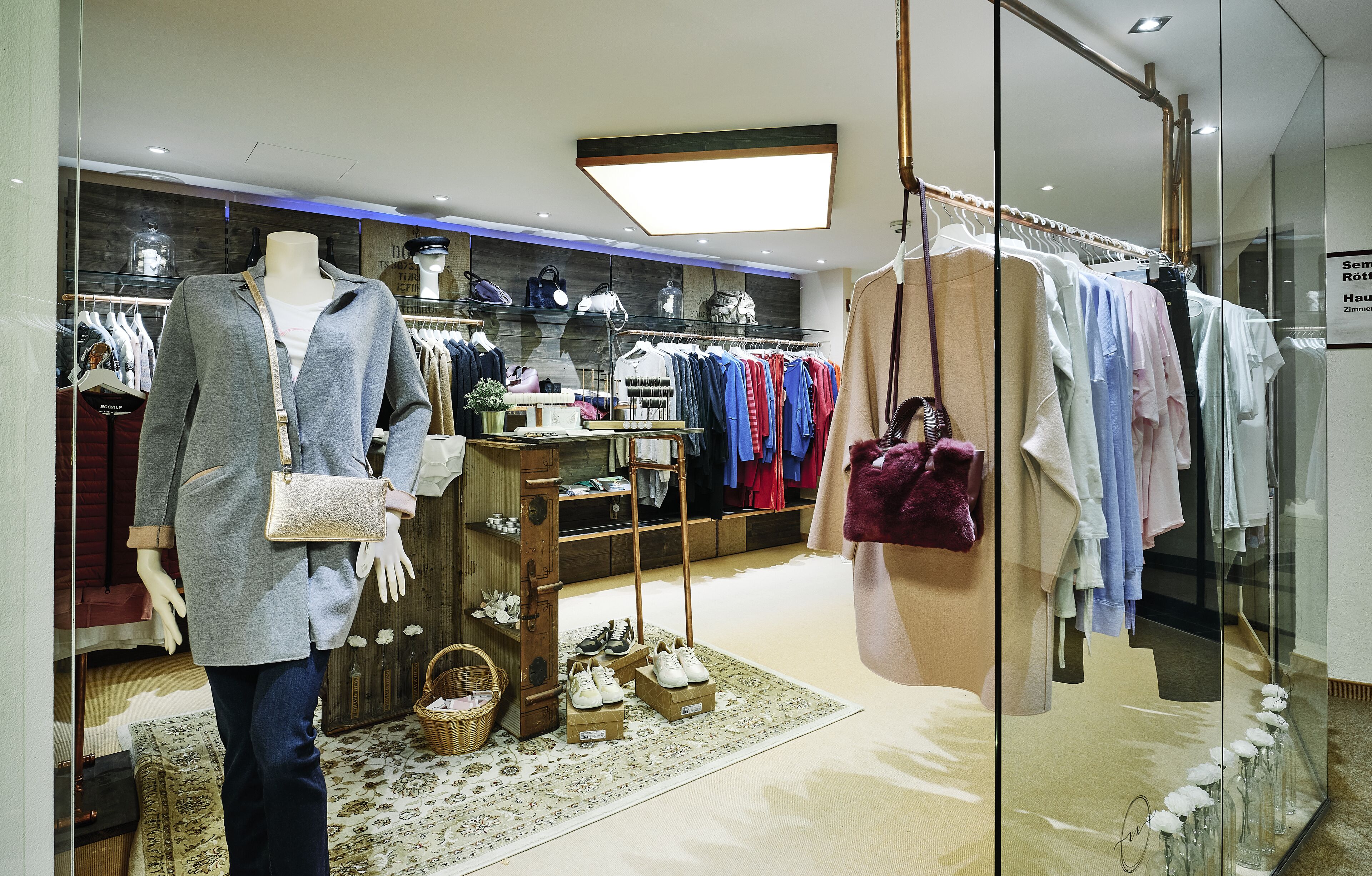 A clothing store with a mannequin, racks of clothes, and a display of shoes.
