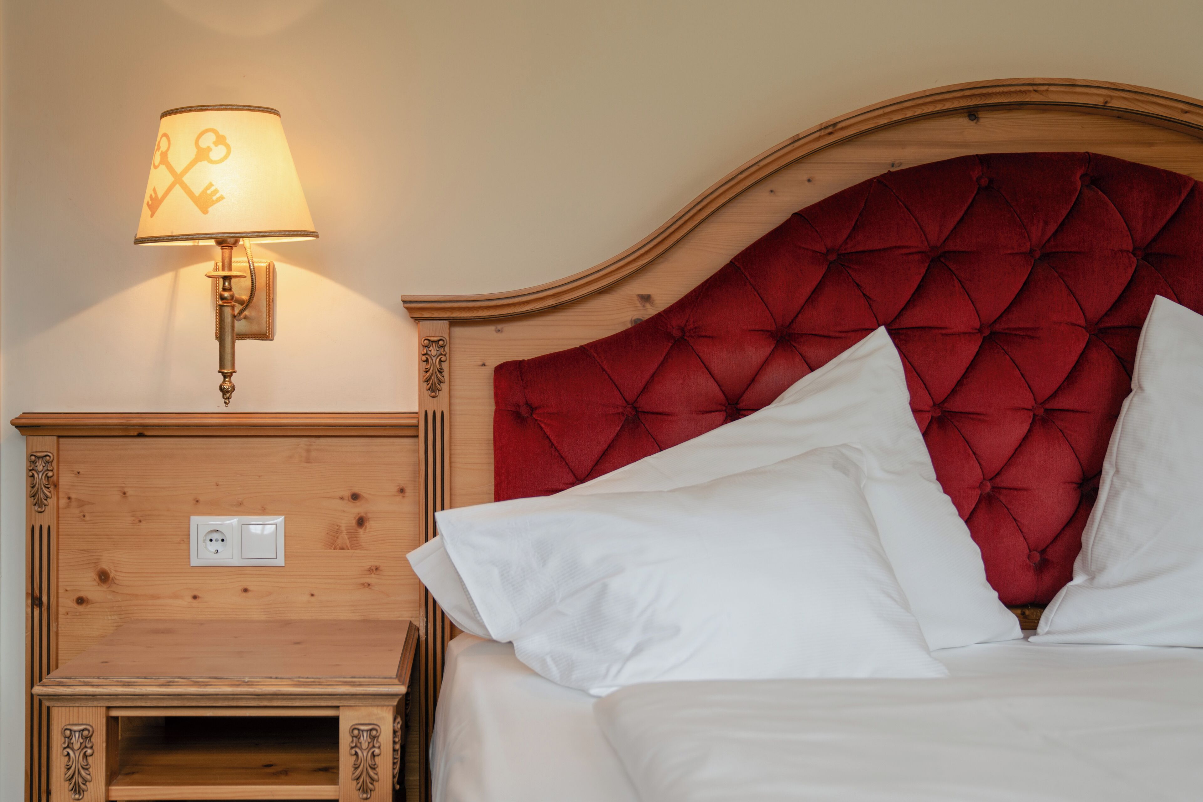 A neatly made bed with white linens and a red tufted headboard.