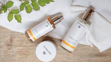 Two bottles of Dr. Hauschka skincare products and a container on a wooden surface with a white cloth.