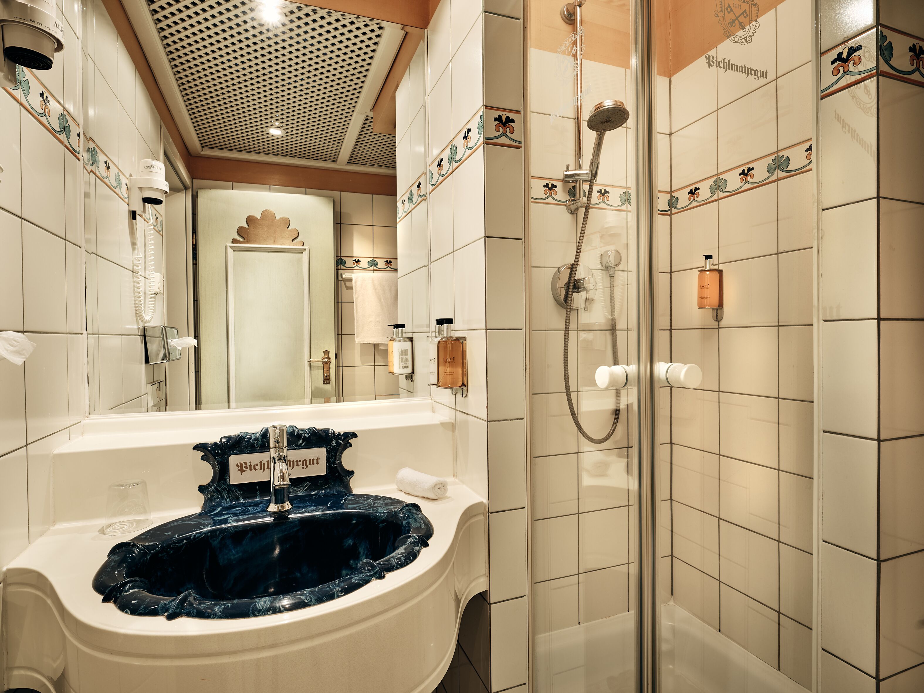 A bathroom with a sink, mirror, shower, and tiled walls.