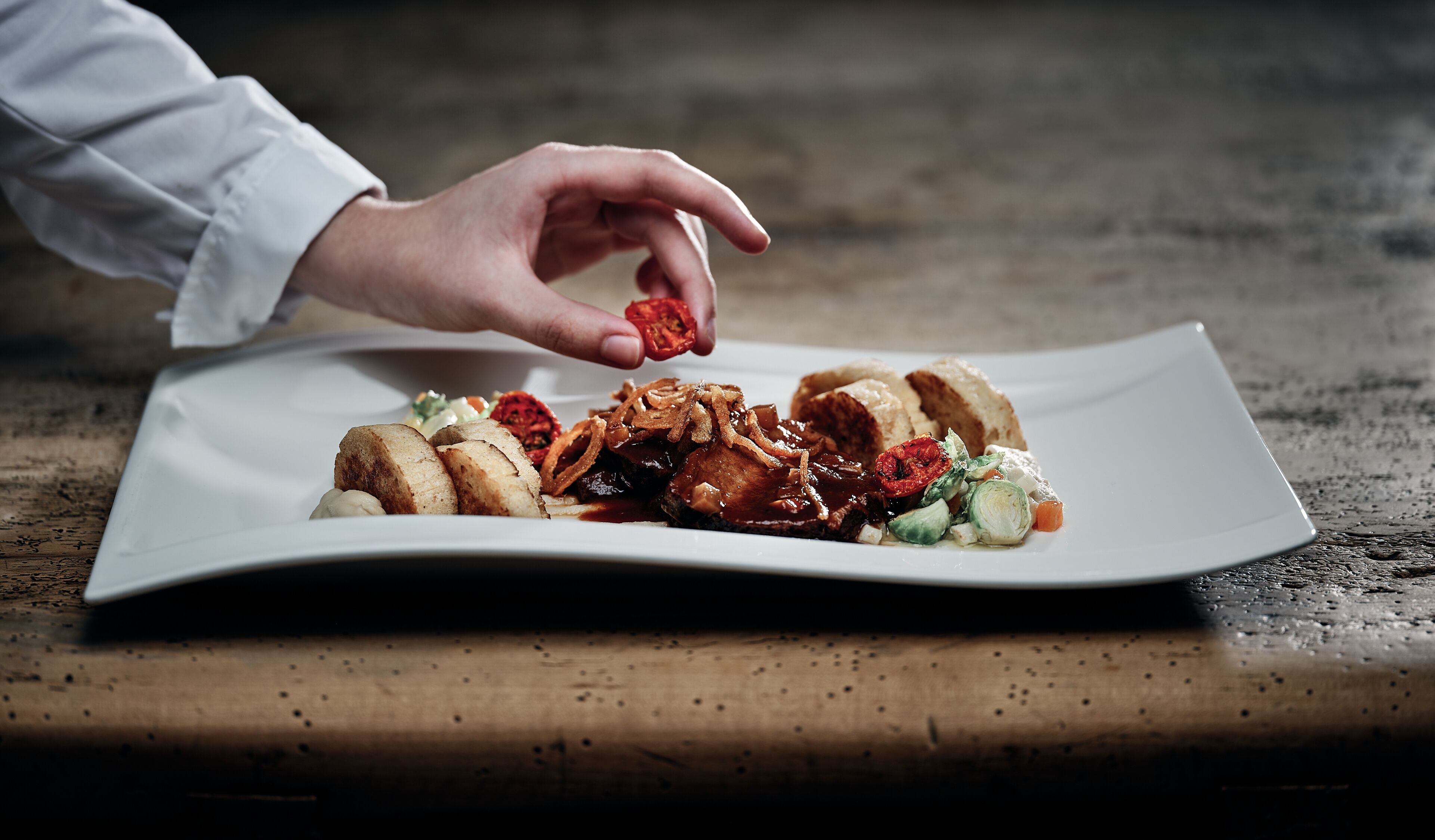 A plate of food with a hand adding a garnish.