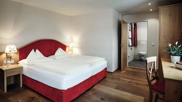 A modern bedroom with a red upholstered bed, bedside lamps, a wooden nightstand, a wooden desk with a chair, and a potted plant.