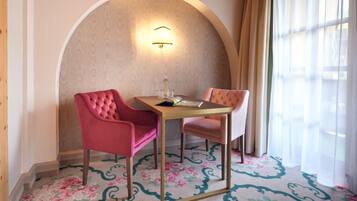 Habitación de hotel con una pequeña mesa, dos sillas, alfombra estampada y un ventanal con cortinas.