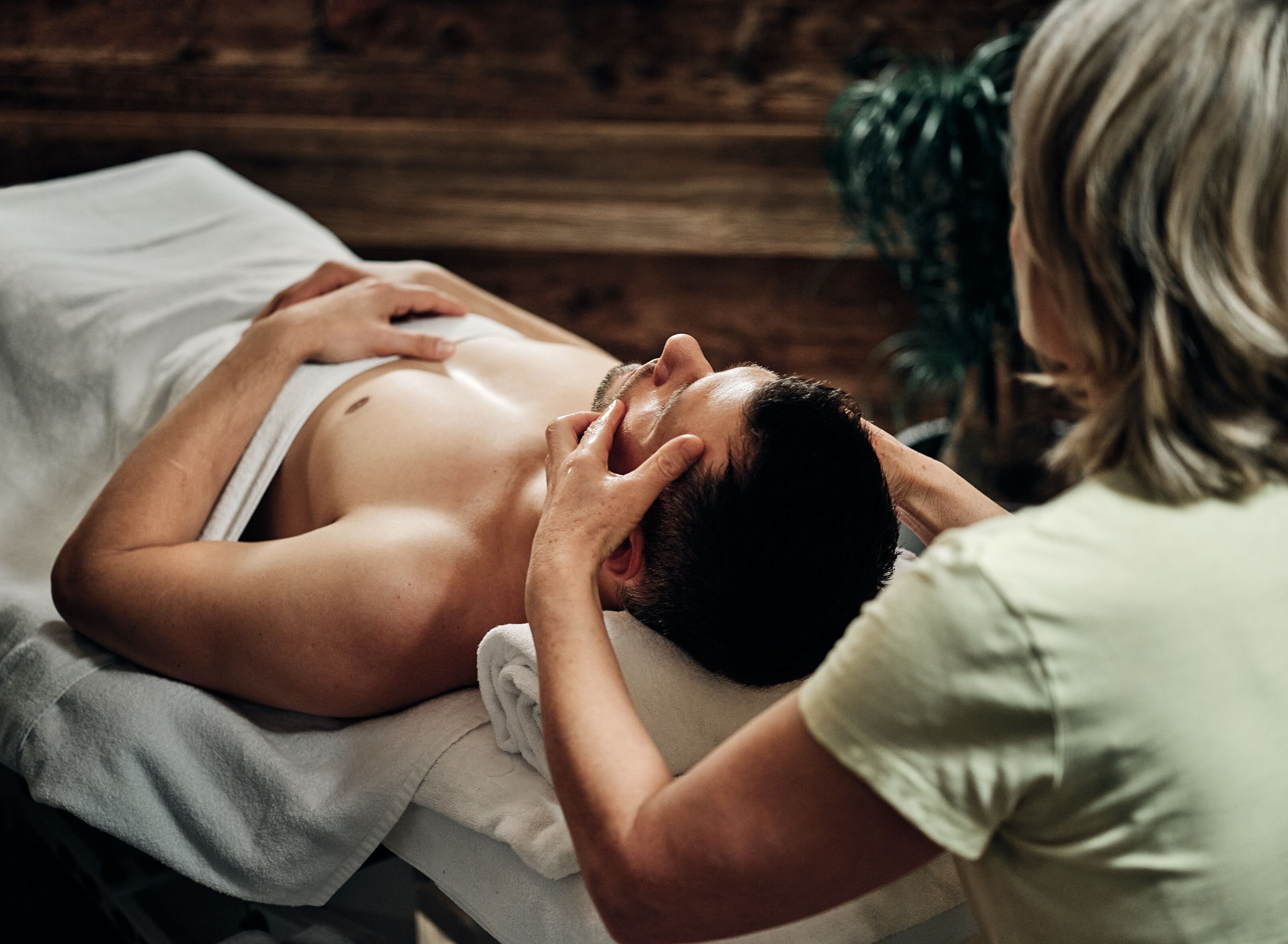 A person receiving a massage in a room with a wooden wall and a plant in the background.