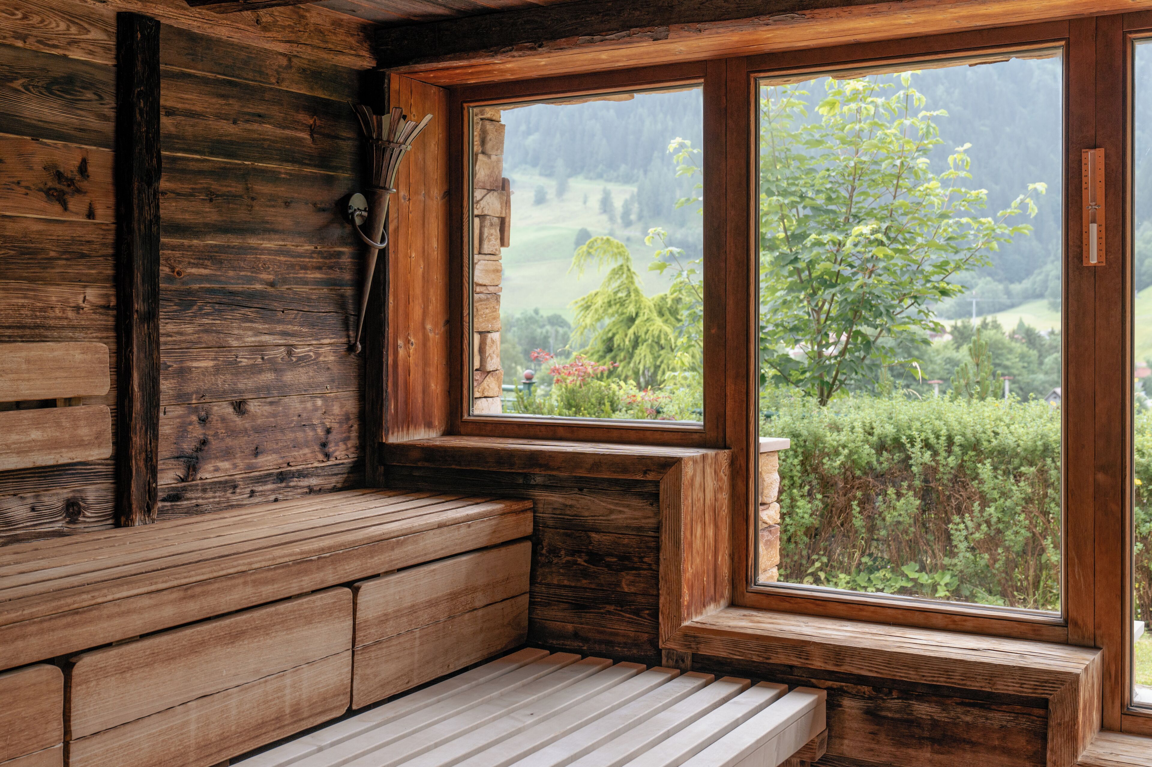 A wooden bench with a view of a green landscape through a large window.