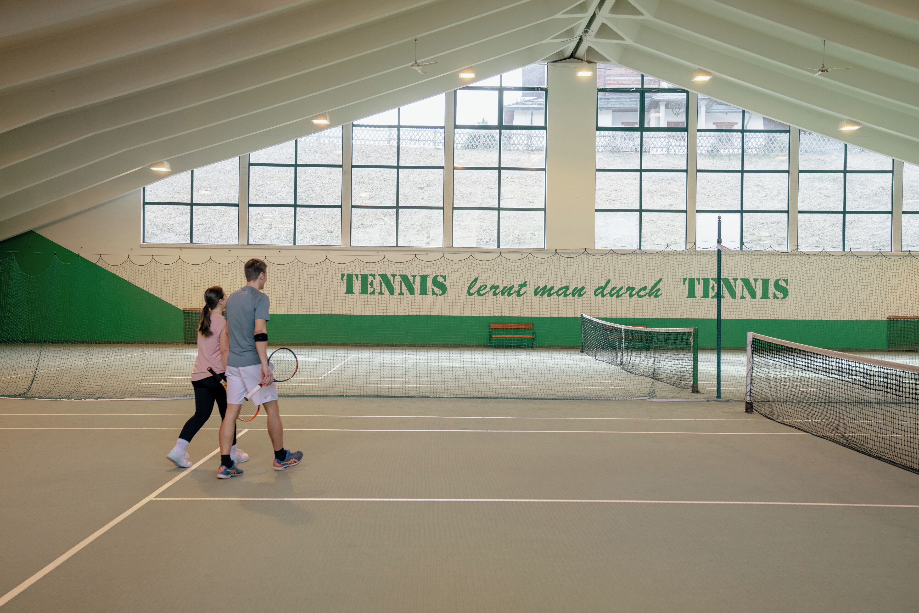 Un court de tennis intérieur avec un filet, un banc et un mur sur lequel est écrit le mot « TENNIS ».