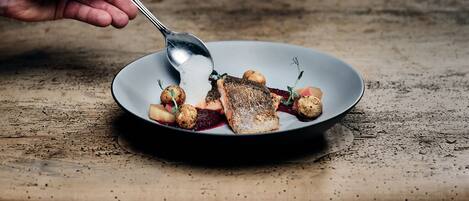 A hand holding a spoon over a plate with food, on a rustic wooden surface.