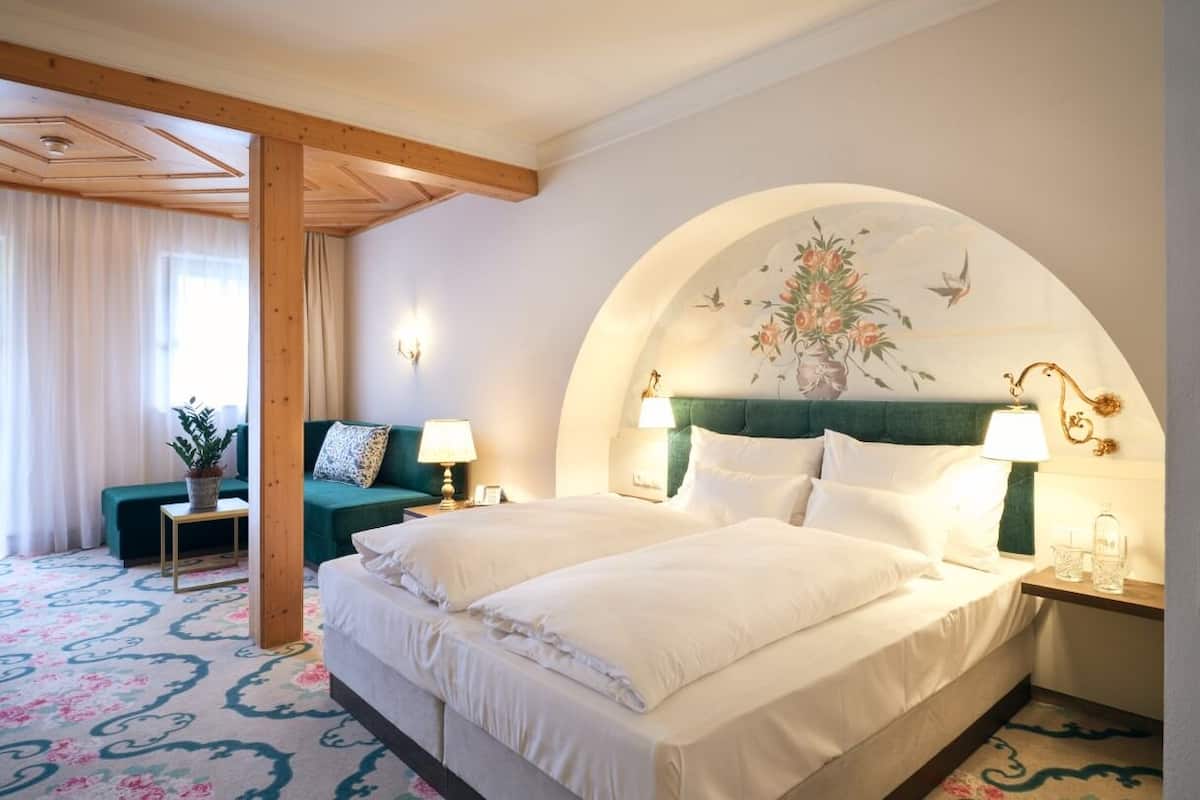 A hotel room with a large bed, a green sofa, a small table with a lamp, and a decorative wall arch.