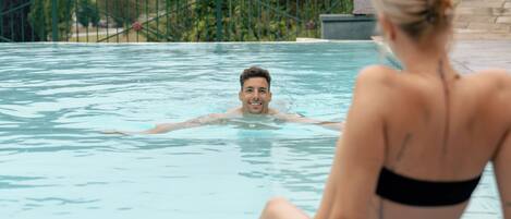 Una piscina con una persona nadando y otra sentada en el borde.
