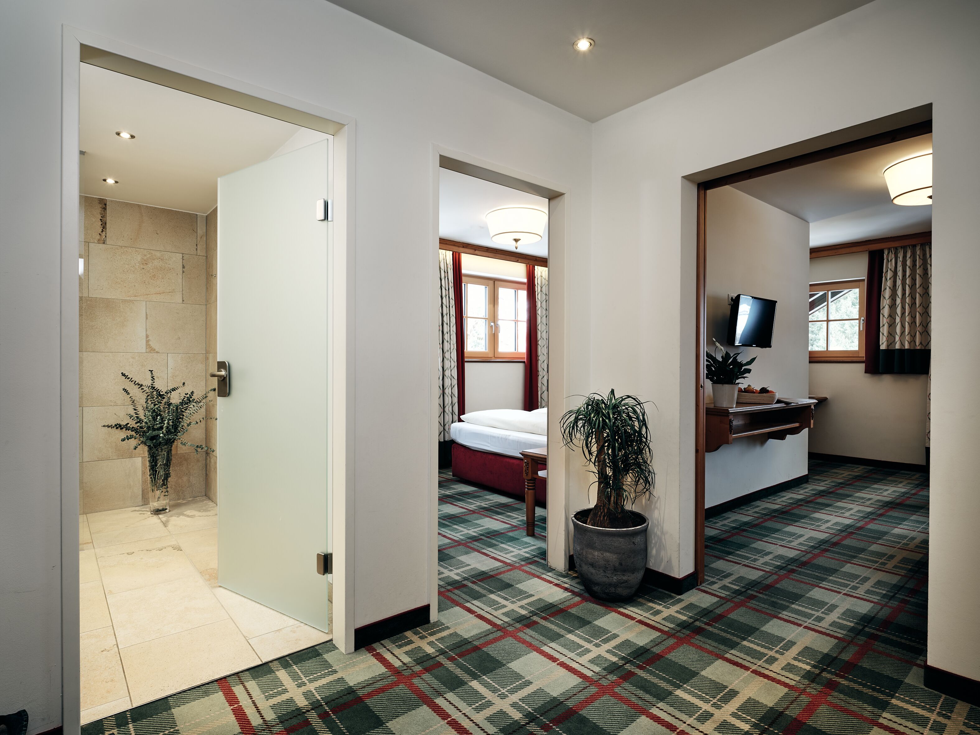 A hotel hallway with a checkered carpet, a potted plant, and a television on a stand.