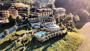 Un hotel grande de varios pisos con piscina, rodeado de exuberante vegetación y colinas.
