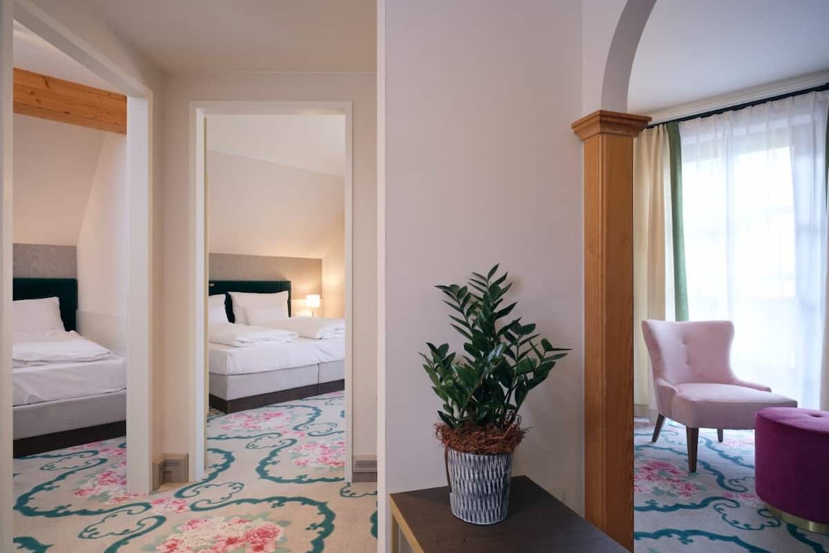 A hotel room with a bed, a bedside table with a plant, a chair, and a window with curtains.