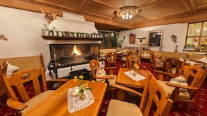 A cozy dining area with wooden furniture, a fireplace, and a red carpet. - Sittnerhof (Merano)