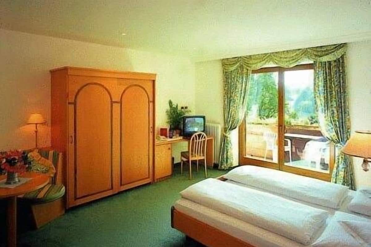 A hotel room with a bed, a desk, a chair, a TV, and a view of the outdoors.