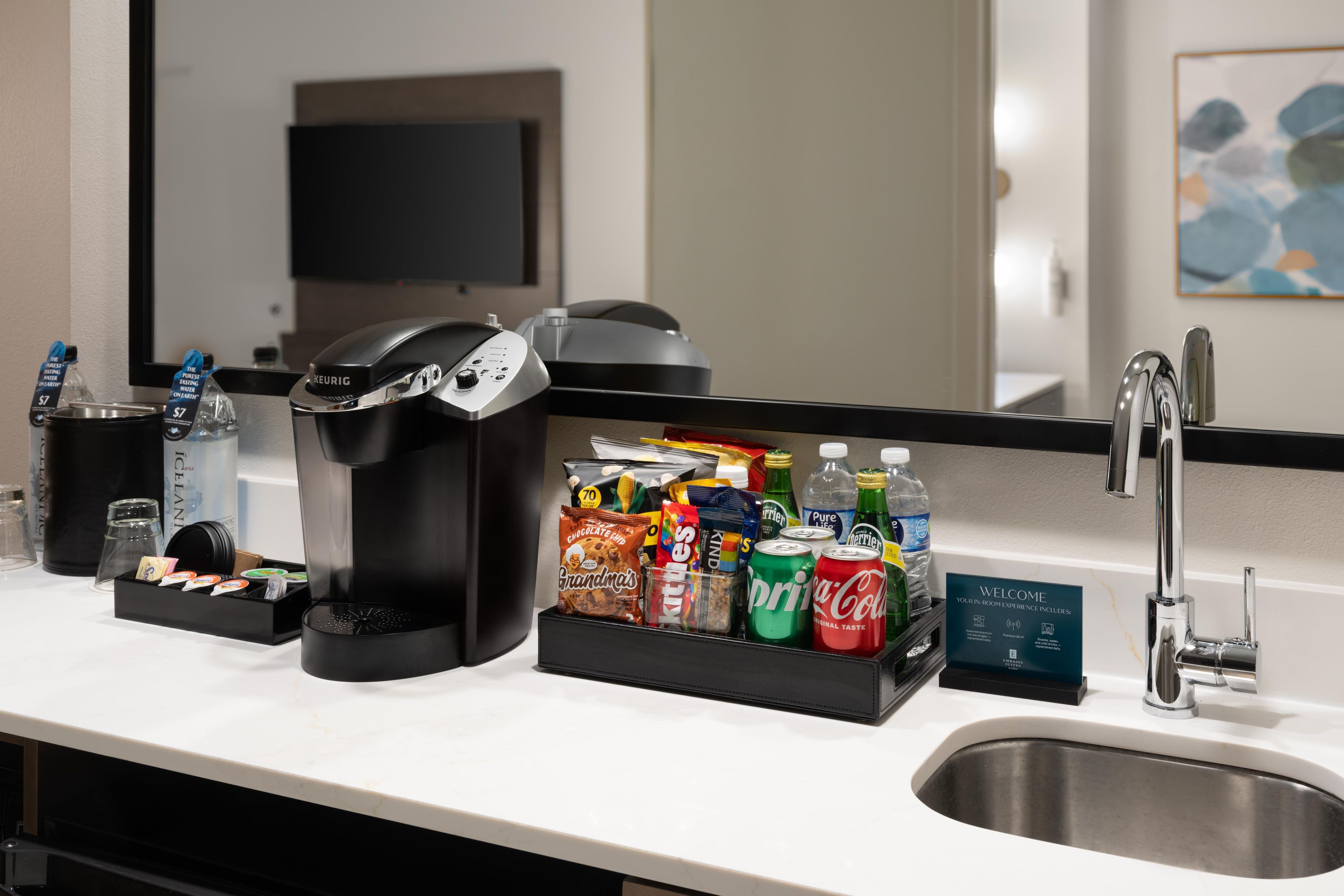 Ett hotellrum med en kaffebryggare, en dryckesautomat, en snackbar och ett handfat.