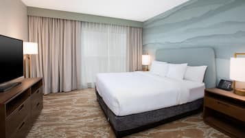 A hotel room with a large bed, a flat-screen TV, a desk with a lamp, and a wall-mounted phone.