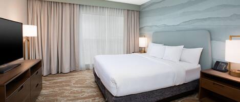 A hotel room with a large bed, a flat-screen TV, a desk with a lamp, and a wall-mounted phone.