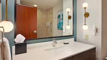 A bathroom with a white sink, a mirror, and a shower. There are toiletries on the sink and a towel rack.