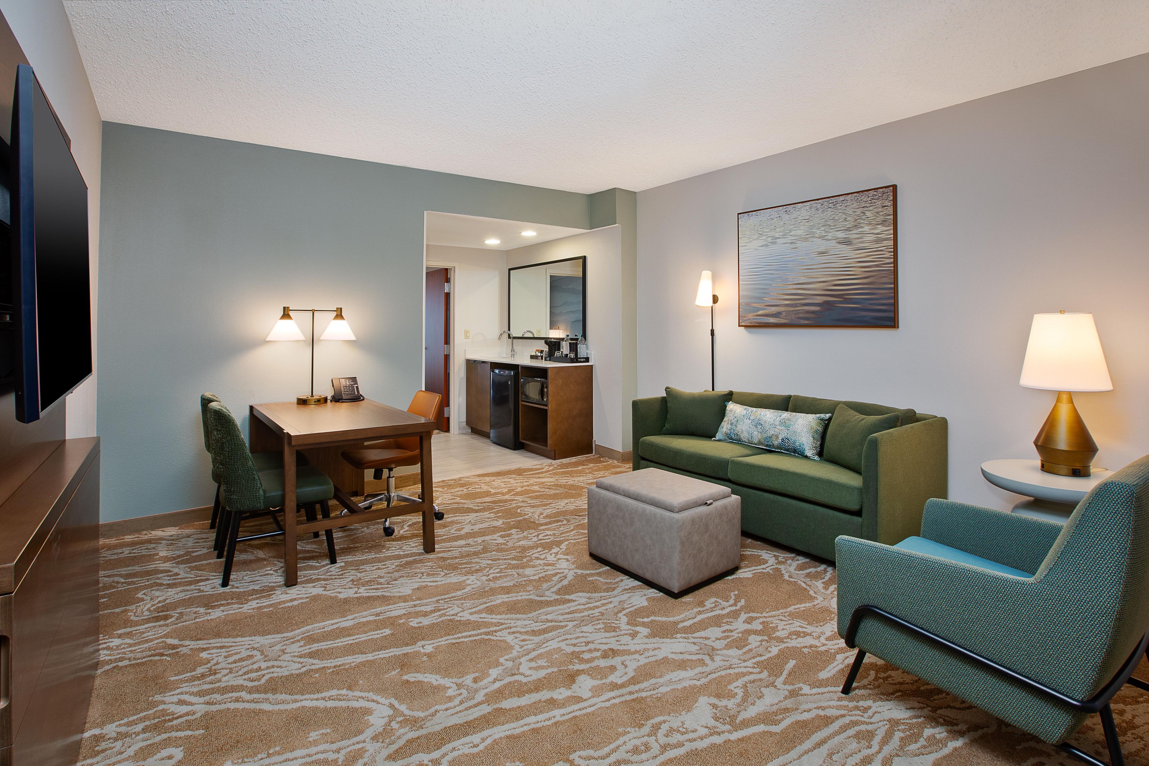 Une chambre d’hôtel comprenant un coin repas, un canapé, un fauteuil, une télévision et un tableau au mur.