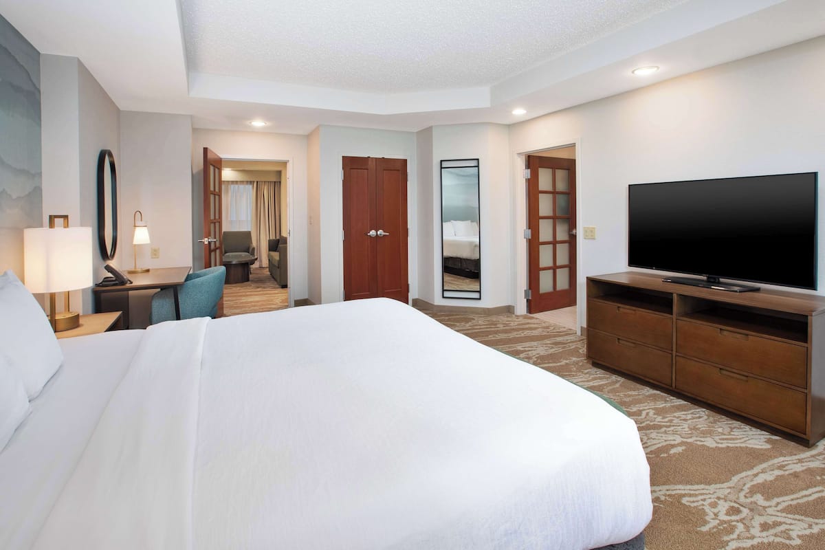 Een hotelkamer met een groot bed, een televisie, een bureau met lamp en een spiegel.