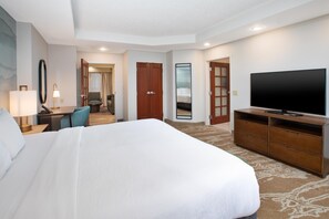 Habitación de hotel con una cama grande, televisor, escritorio con lámpara, una silla y un espejo.
