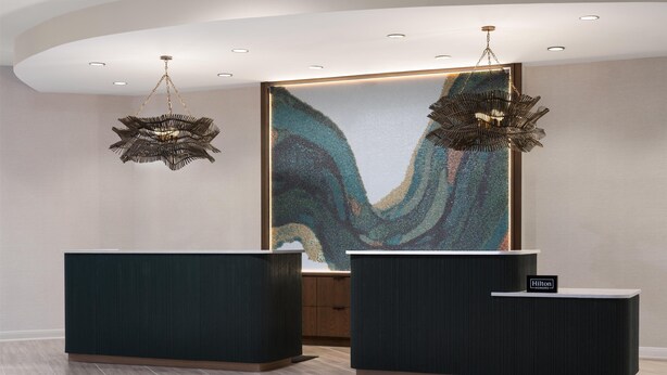 A reception area with two dark reception desks, a large abstract artwork on the wall, and two unique hanging light fixtures.