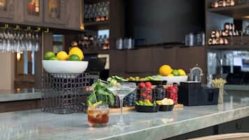 Una zona de bar con encimera de mármol, un bol de frutas, una copa de martini y una bebida con una rodaja de limón.