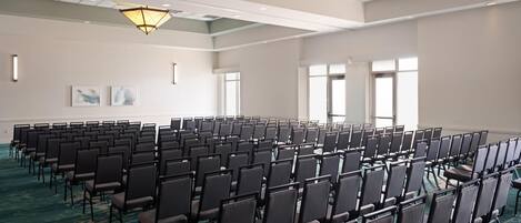 Uma sala de conferências com fileiras de cadeiras, janelas amplas e piso coberto de carpete.