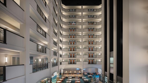 Um saguão de hotel em vários níveis, com um átrio central, diversas áreas de refeições e uma piscina.