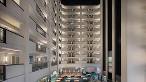 A multi-level hotel lobby with a central atrium, multiple dining areas, and a pool.