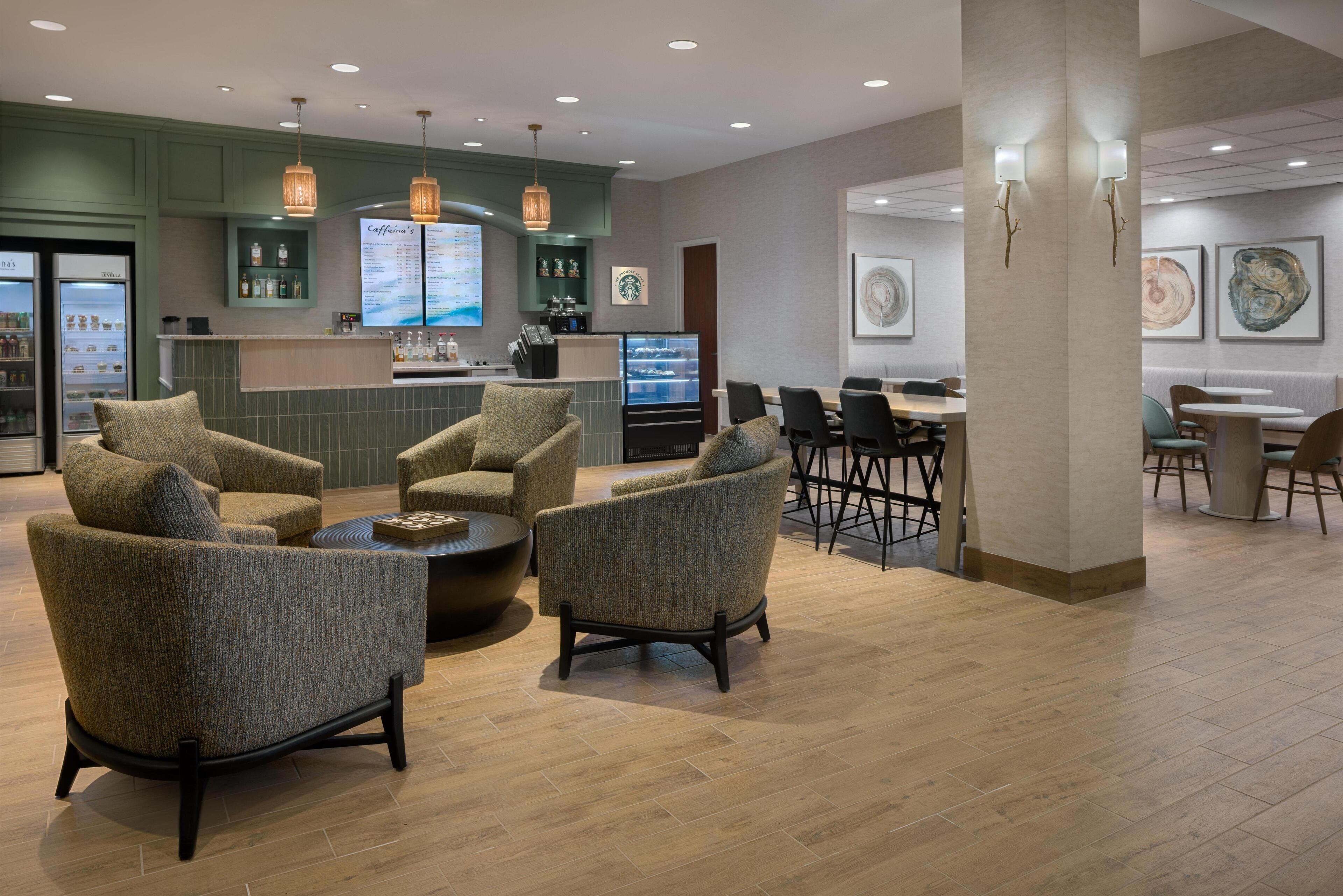 A modern lounge area with seating, a coffee station, and a digital menu board.