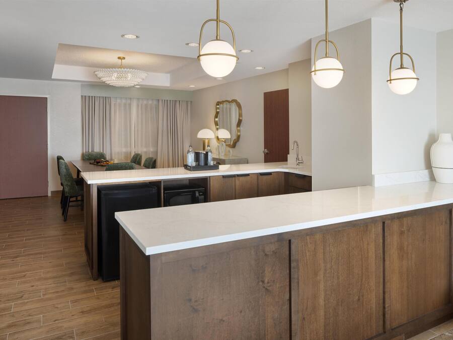 A modern kitchen with a central island, pendant lighting, and a dining area with chairs.