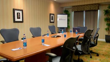 A conference room with a long table, multiple chairs, a projector screen, and framed pictures on the wall.