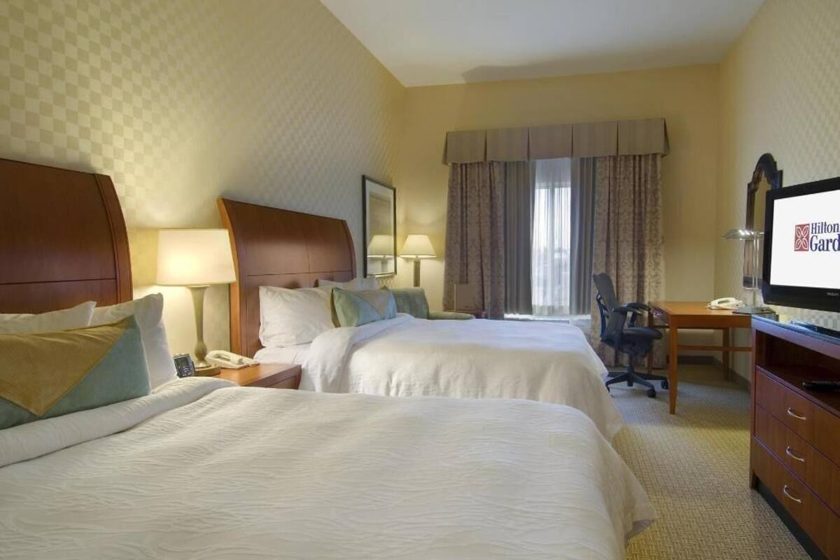 A hotel room with two beds, a desk with a computer, a telephone, and a television.