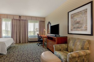 Habitación de hotel con cama, escritorio con televisor, silla, sofá y ventana con cortinas.