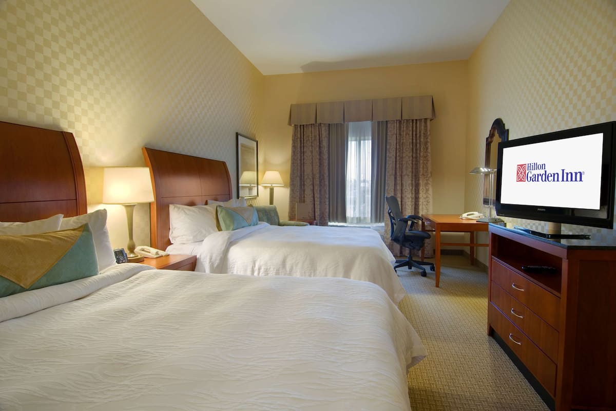 A hotel room with two beds, a desk, a television, and a telephone.