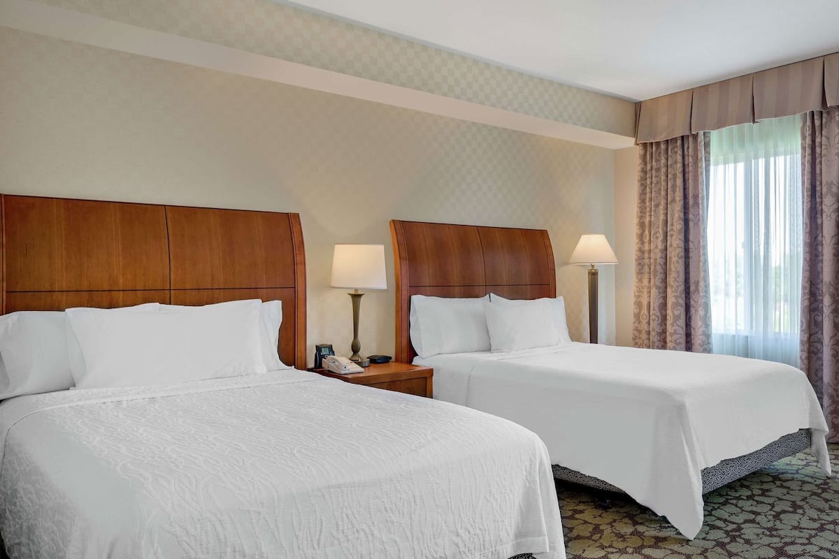 A hotel room with two beds, wooden headboards, bedside lamps, a telephone, and a window with curtains.
