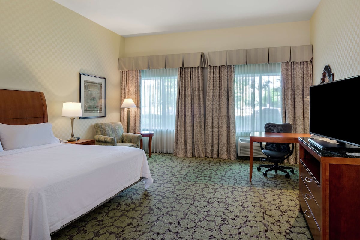 A hotel room with a large bed, a desk with a chair, a television, and a window with curtains.