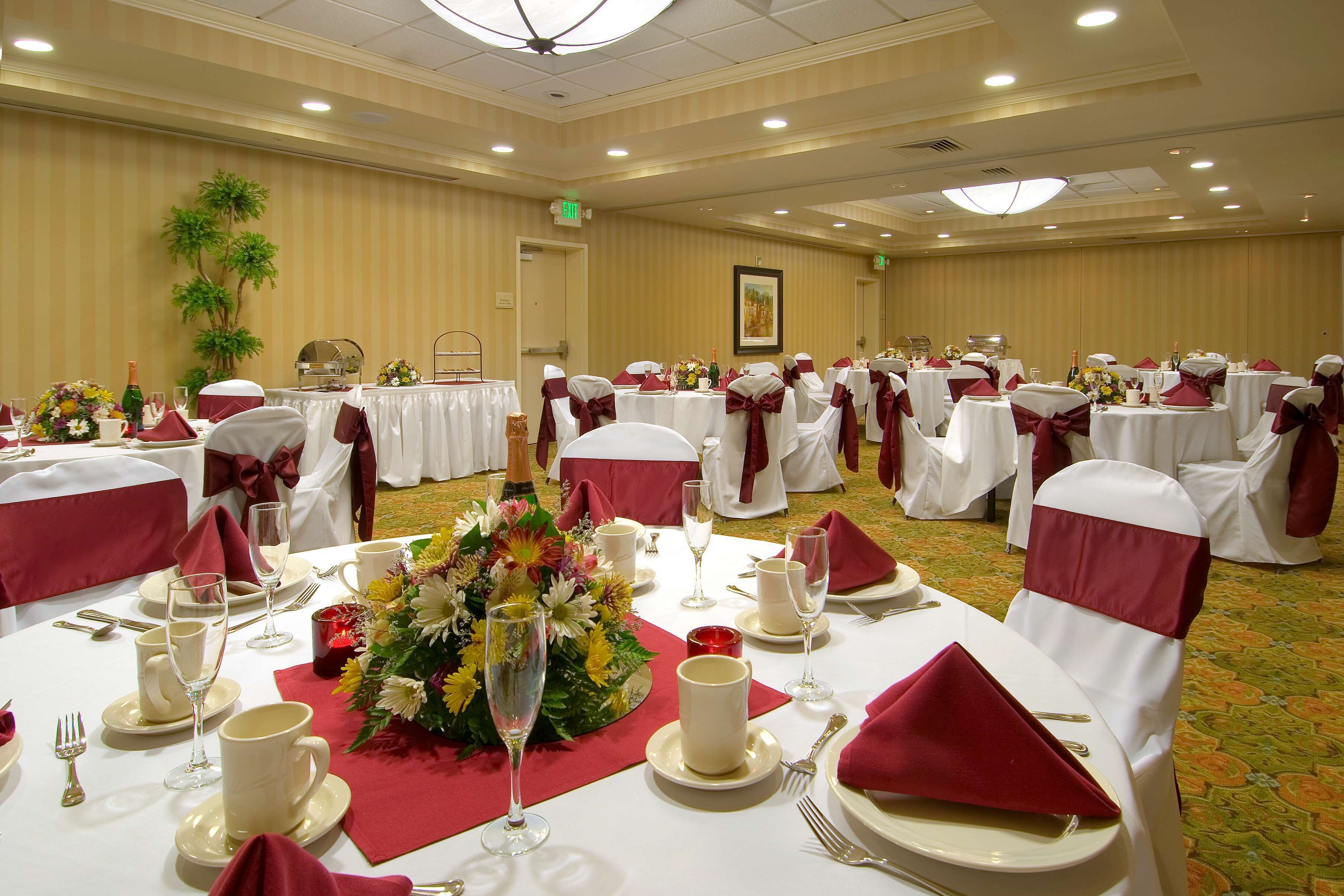 A banquet hall with round tables set for a formal event, featuring white tablecloths, red napkins, and floral centerpieces.