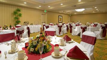 A banquet hall with round tables set for a formal event, featuring white tablecloths, red napkins, and floral centerpieces.